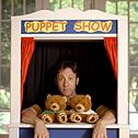 A man with 2 teddy bears in a puppet show booth